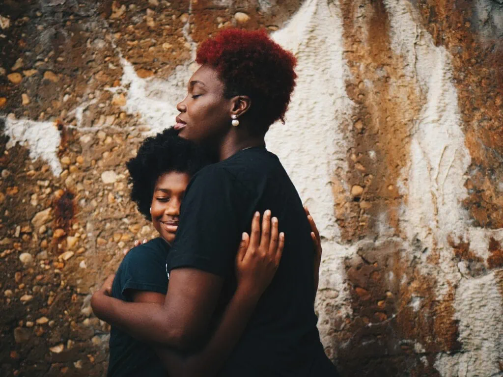An image of a young black girl and her mother embracing in a loving hug, after coming out to her family.