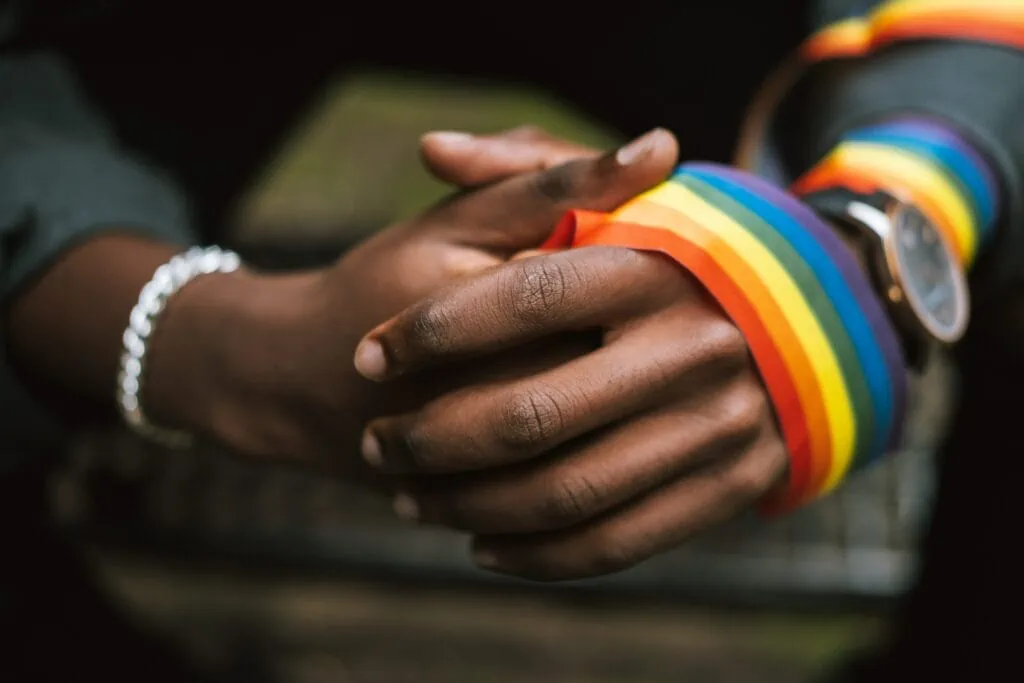 A black queer person wearing a rainbow ribbon around their hands after coming out at school.