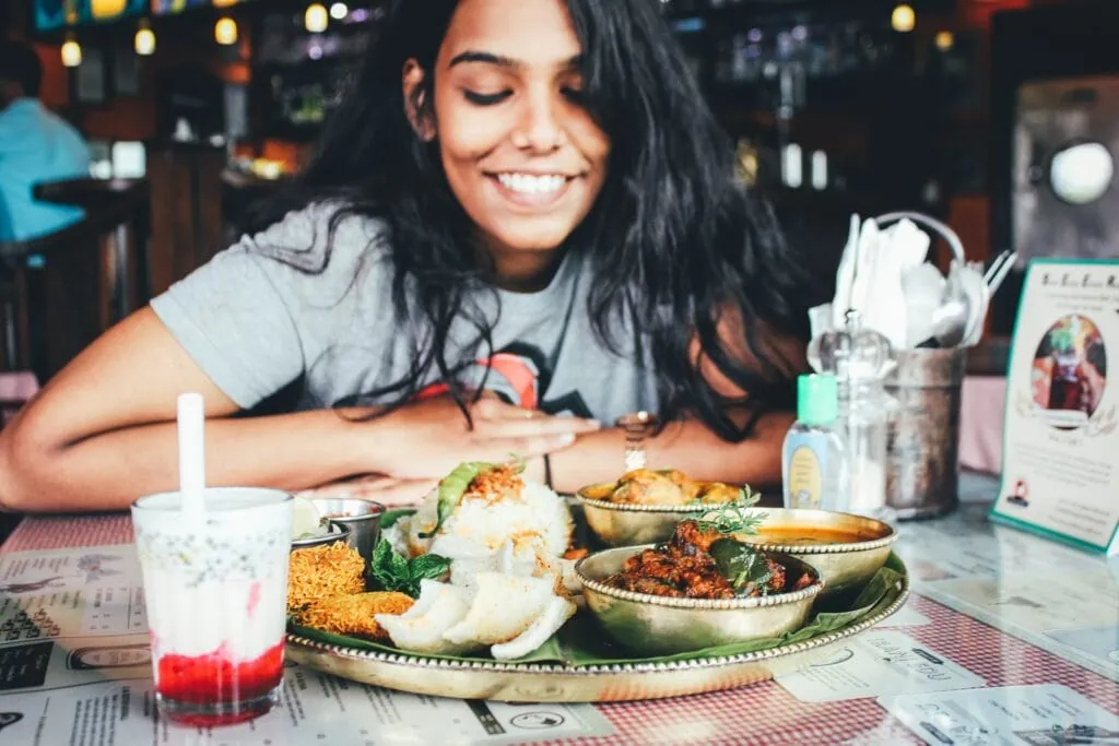 A woman smiles looking at food on the table as she goes on a food crawl with her queer date.