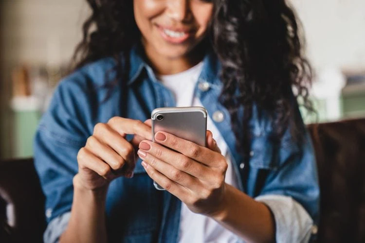 A woman holding a phone, we only see the bottom half of her face and she’s smiling.