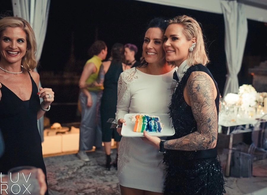 Posing together and smiling with a slice of rainbow wedding cake