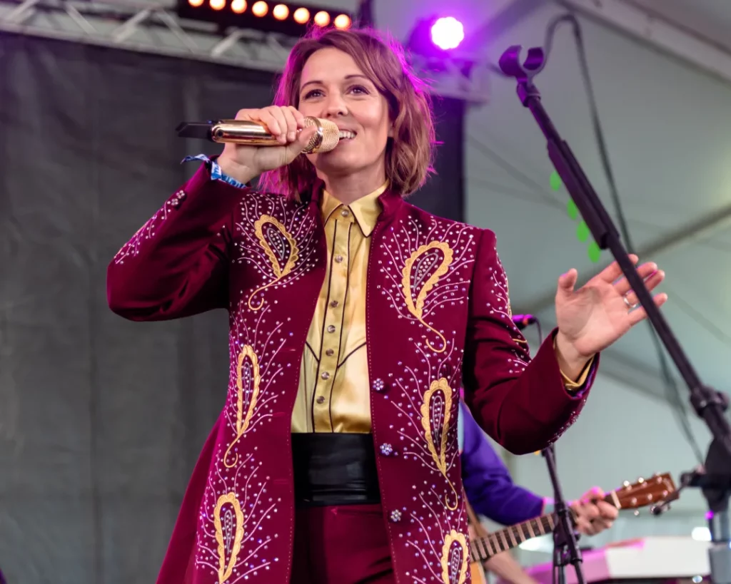 Brandi Carlile on stage with a golden microphone to match her gold and burgundy outfit