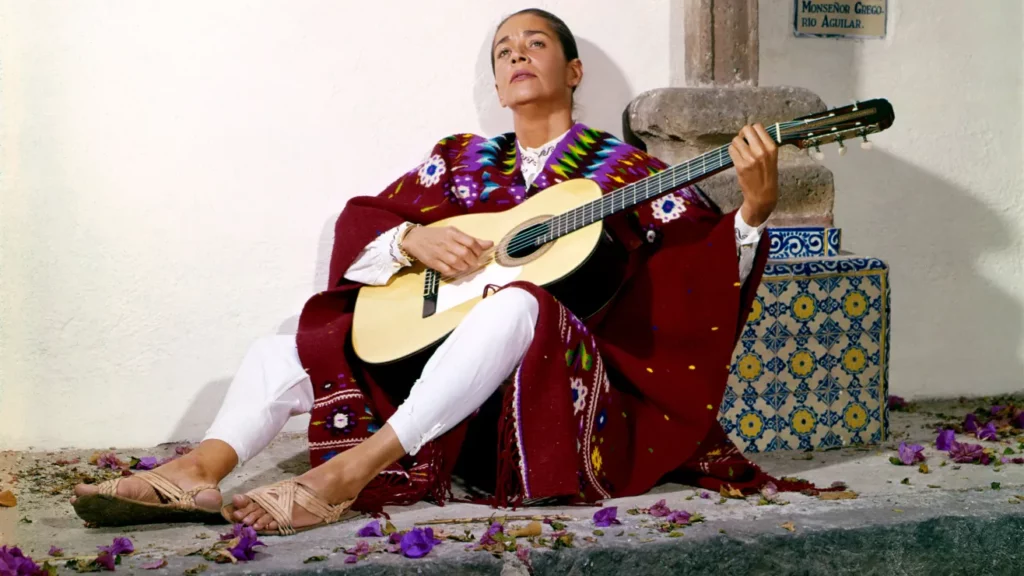Chavela Vargas sitting on a sidewalk with her guitar.