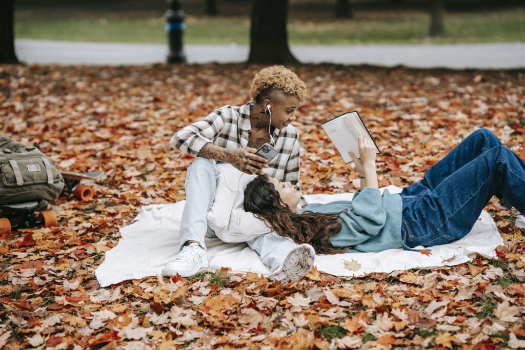 Un couple lesbien multiracial - comprenant une lesbienne Stud - est allongé sur une couverture au-dessus des feuilles d'automne.