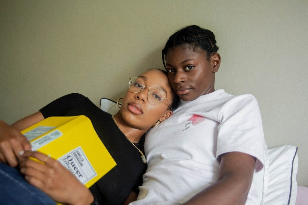 A lesbian couple read a book in bed together.