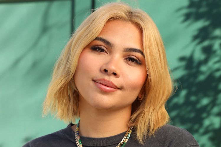 Hayley Kiyoko posing against a green backdrop, smiling for a photo shoot with Trevor Flores, while promoting a new album.