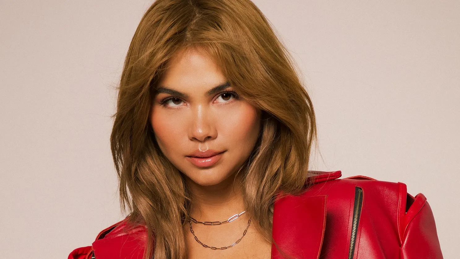 Hayley Kiyoko posing against a green backdrop, smiling for a photo shoot with Trevor Flores, while promoting a new album.
