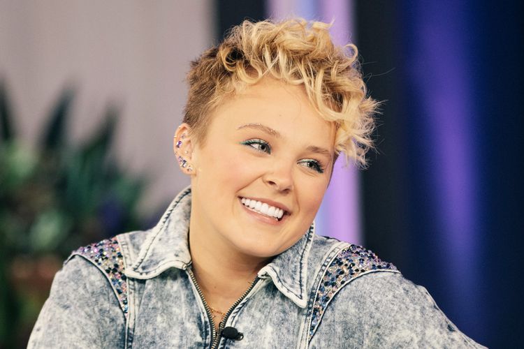 Jojo Siwa rocking a short, curly pixie cut, smiling happily, showing off her perfect smile!