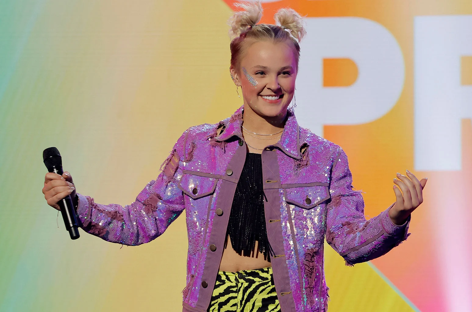 Jojo Siwa rocking a short, curly pixie cut, smiling happily, showing off her perfect smile!