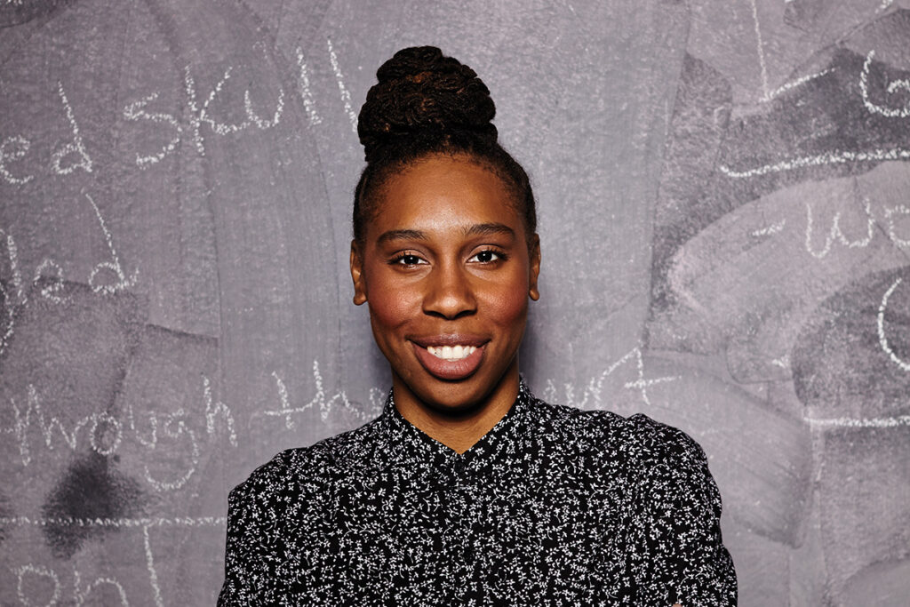 Lena Waithe posing for a portrait in front of a chalkboard, while wearing a floral top.