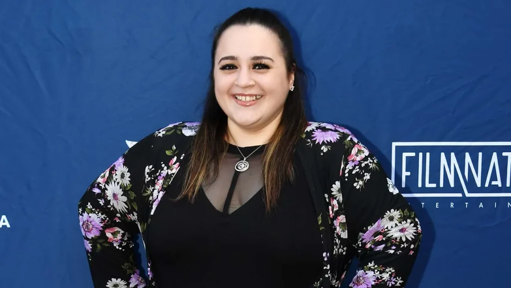 Nikki Blonsky wearing a floral cardigan and posing at an event, looking stunning as ever.