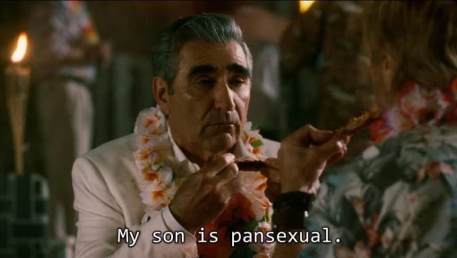Johnny Rose, David Rose’s father portrayed by Eugene Levy, is seen in this screenshot saying “My son is pansexual” while eating ribs with a lei around his neck. David, portrayed by Dan Levy, is openly pansexual and has relationships with both men and women throughout the series.