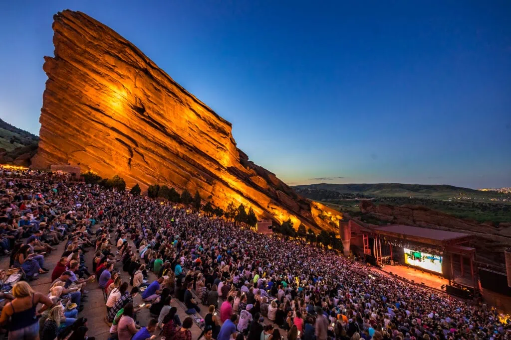 The Denver film festival sometimes screens its movies at the Red Rocks Amphitheater, an open-air amphitheater built into a rock structure, seen here, with seemingly hundreds of people watching a screening at sunset.
