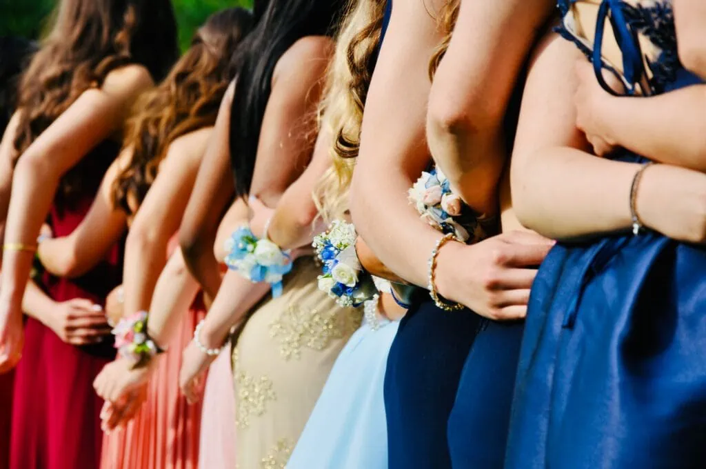 Women wearing sleeveless dresses of varying colors with carnations on their wrists, presumably ready for prom.