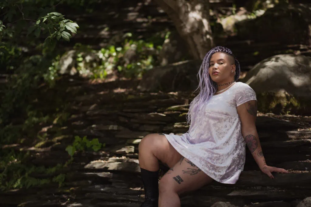 A nonbinary, queer Afro-Latinx person exudes confidence in a dark-lit forest