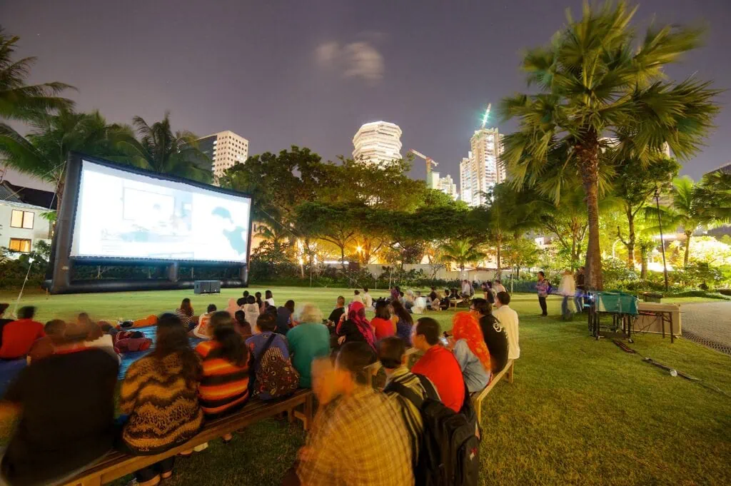 An outdoor film screen in a park with a crowd of people