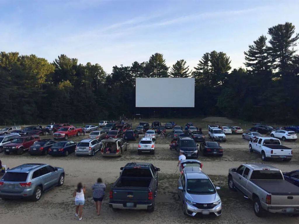 A drive-in movie theater with cars parks and the sun setting in the background.