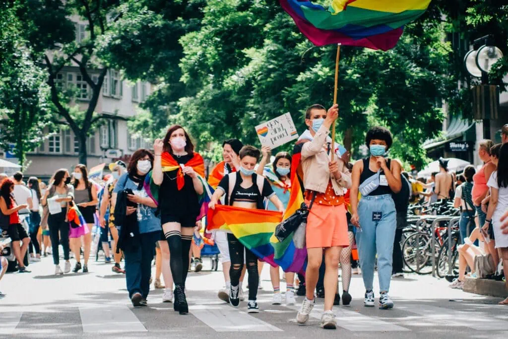 People marching with rainbow flags and Pride signs in the street on a sunny day
