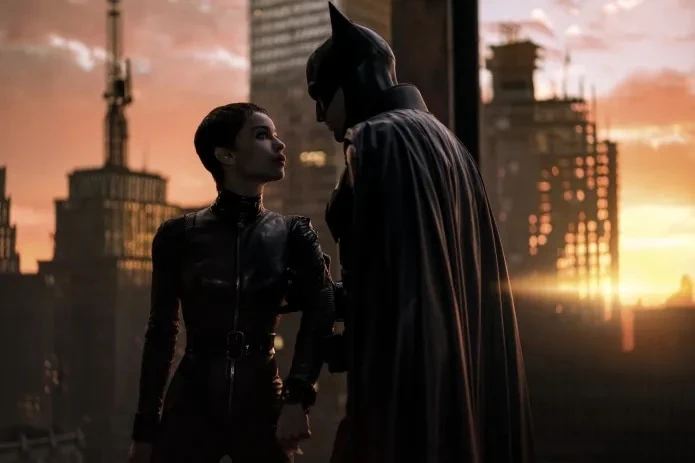 At sunset, Catwoman and Batman face each other in their superhero costumes, with the city of Gotham in the background in a promotional still from the 2022 film The Batman.