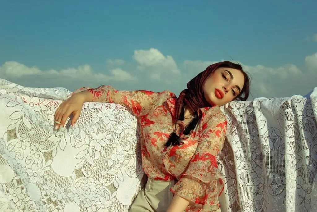 An Iranian person in a colorful blouse posing with a cigarette in hand with a blue sky behind her.