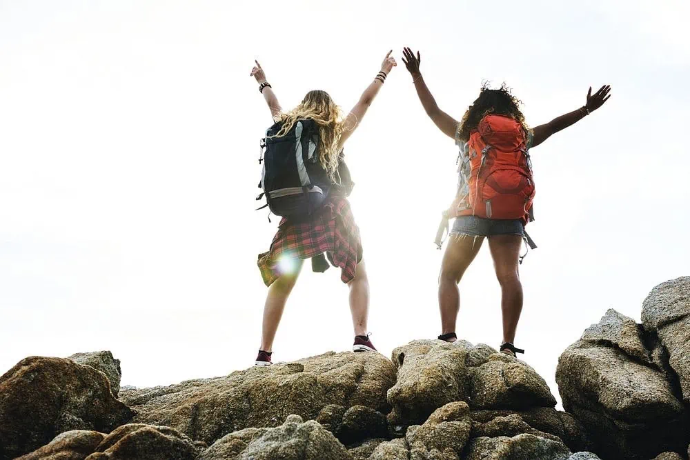 Two hikers raise their arms in celebration on top of boulders.