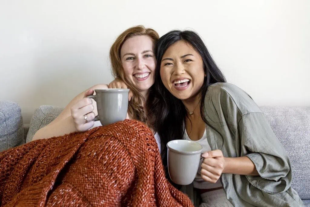 A cozy couple hug on a couch with mugs in their hands.