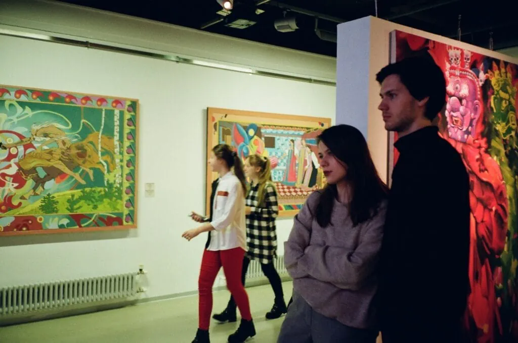 Two couples visit an art gallery where there are a number of artworks hanging on the wall.