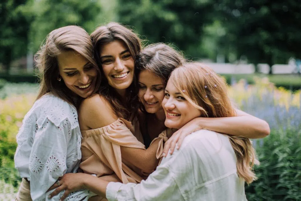 Four women hug and smile in a field, showing a great amount of love and support towards each other.