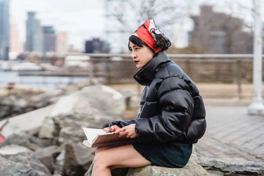 Young person artist admiring river and city and drawing in a sketchbook.
