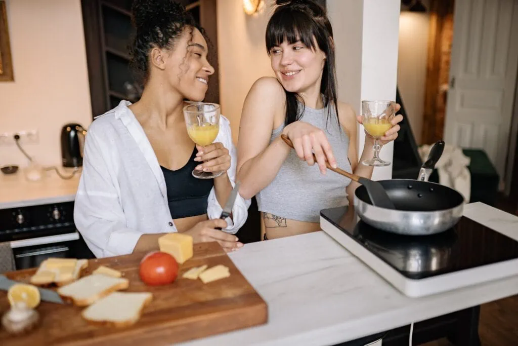 A queer couple cook dinner at home together while drinking.