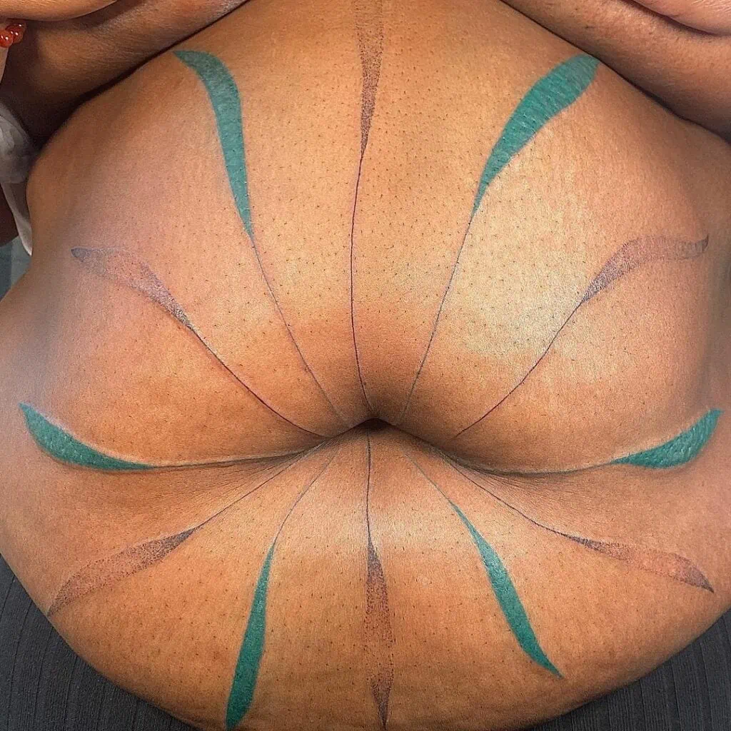 A simple LGBT tattoo of leaves extending from a large black belly by Tiaret Renee 
