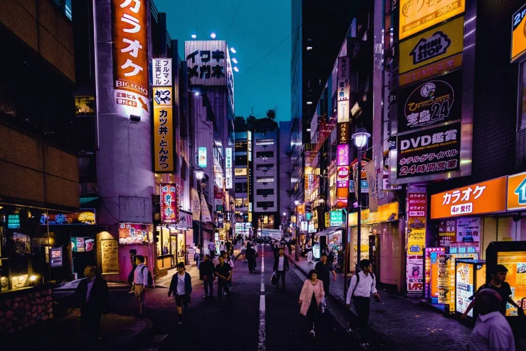 A crowd of people walk down a street in Shinjuku, Tokyo, Japan, during the night.