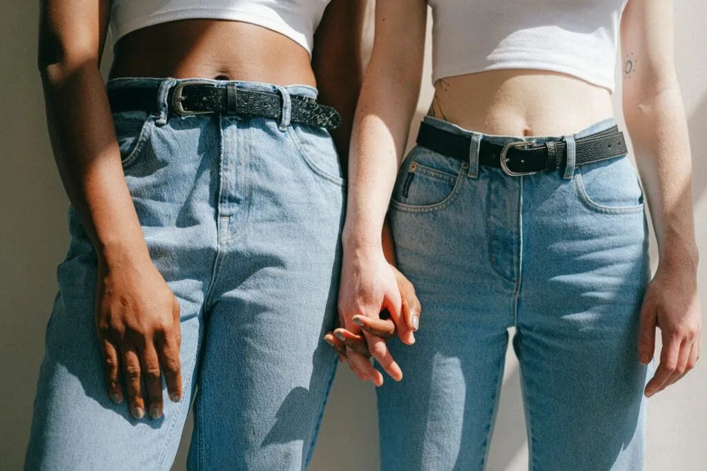 A black queer women and a white queer woman holding hands with blue jeans on