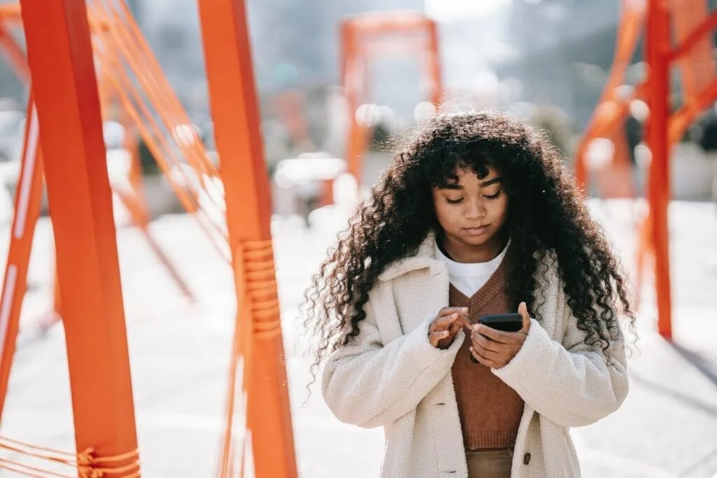 A black woman with curly hair walking on an orange footbridge using a smartphone to call someone.
