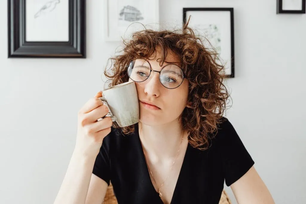 Curly-haired woman holding a mug against her face, probably exhausted from groundhogging in dating.