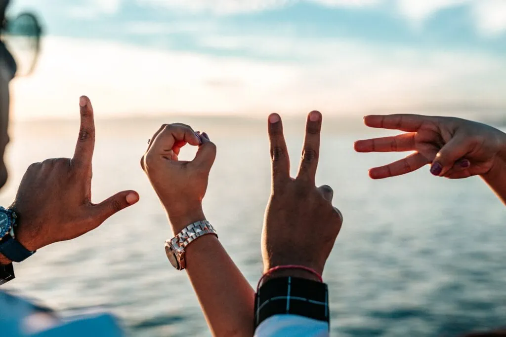 Four hands spell out the word LOVE with their fingers and the beach sea in the background. Being heteroflexible doesn’t mean you’re not worthy of love.