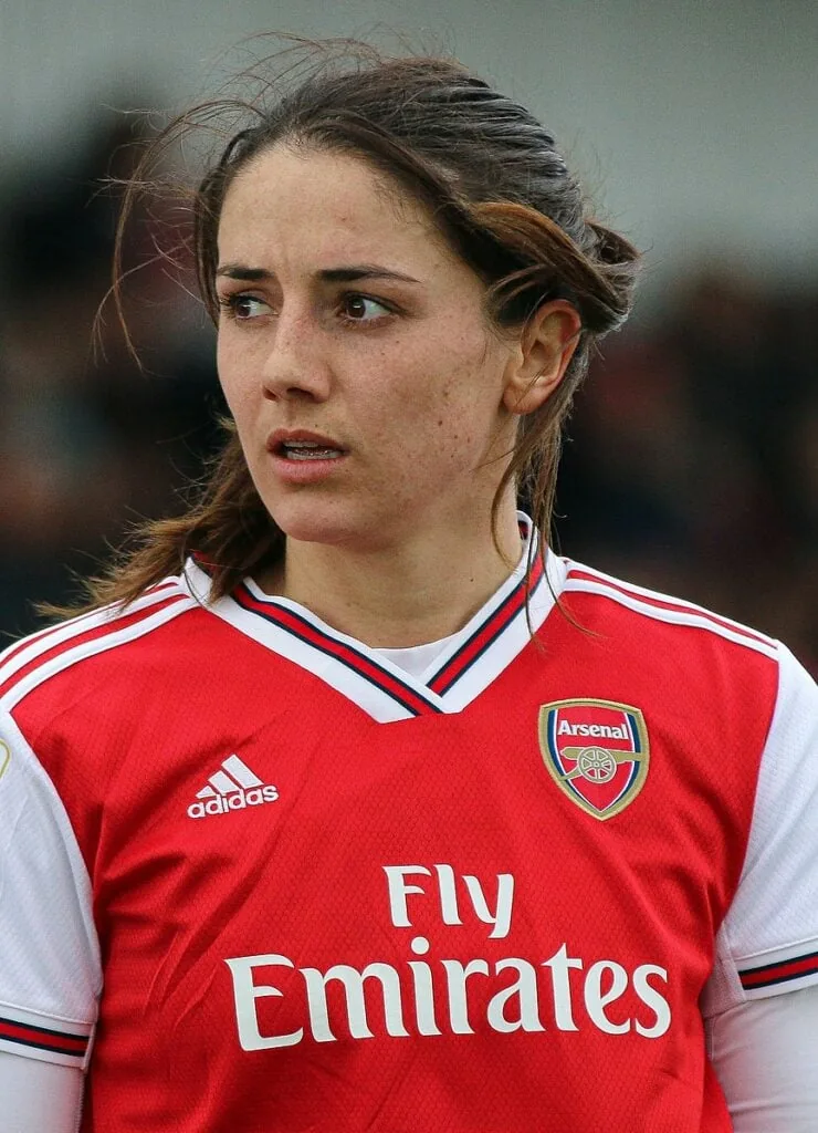 Danielle Van De Donk wearing a red soccer jersey, in the middle of the soccer field, looking out in the middle of a game.