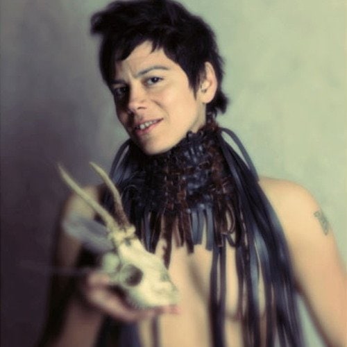 An image of Hilda Viloria taken by Pierre Redon. They are in a leather collar with straps everywhere holding what appears to be an animal skeleton head. The photo is somewhat out of focus.