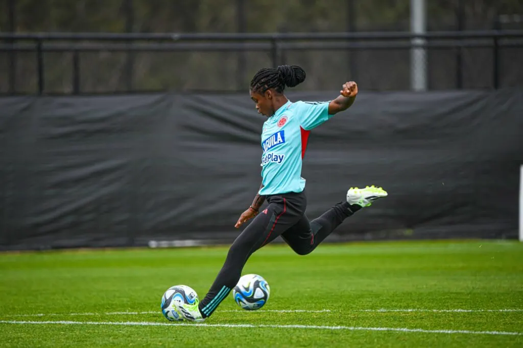 Linda Caicedo on the field as she is about to kick a blue and white soccer ball.