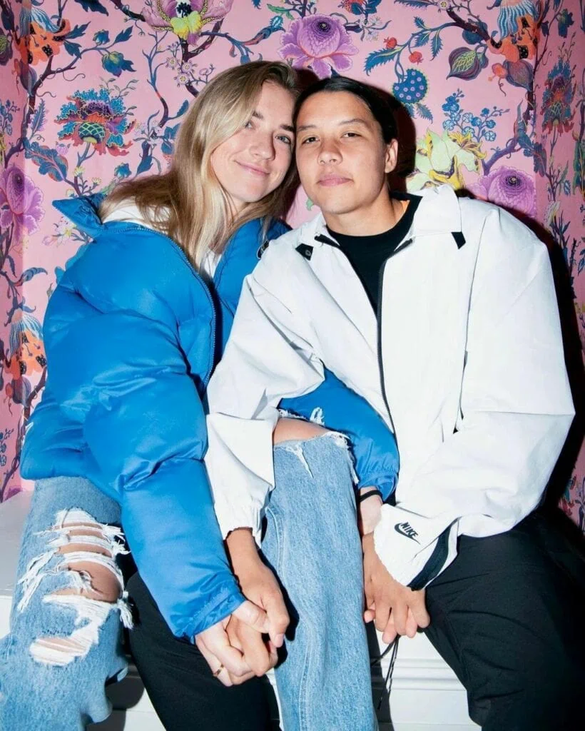 Kristie Mewis smiling against a floral backdrop with her girlfriend, Sam Kerr.