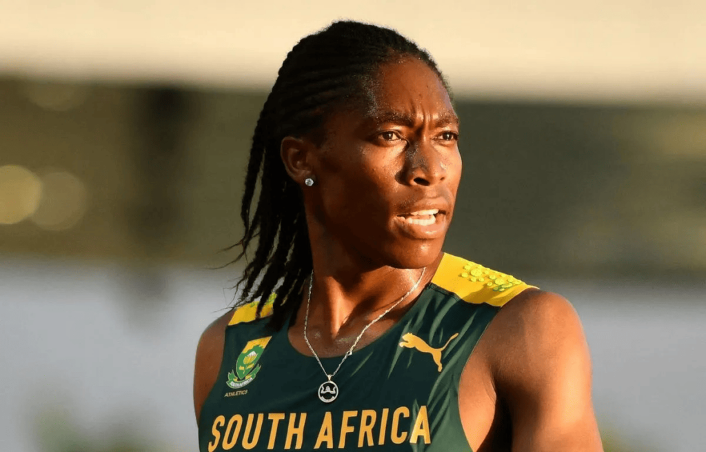 Una imagen de Caster Semenya, mujer negra intersexual y atleta de talla mundial, con una camiseta sudafricana verde y amarilla frente al sol, su piel morena resplandeciente.