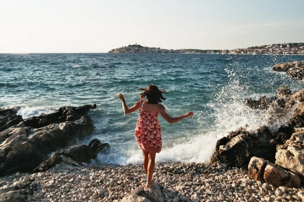 A solo polyamorous woman at the beach standing on the rocks while a wave splashed in front of her.