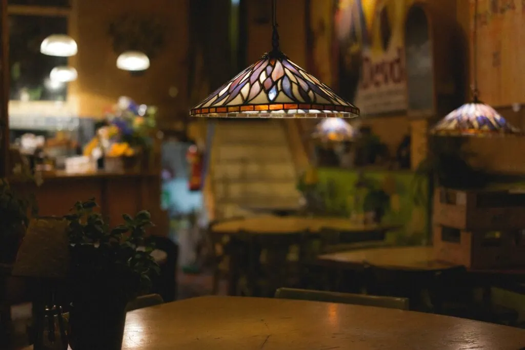 A cozy restaurant with a gorgeous mosaic lampshade hanging over a dimly lit table.