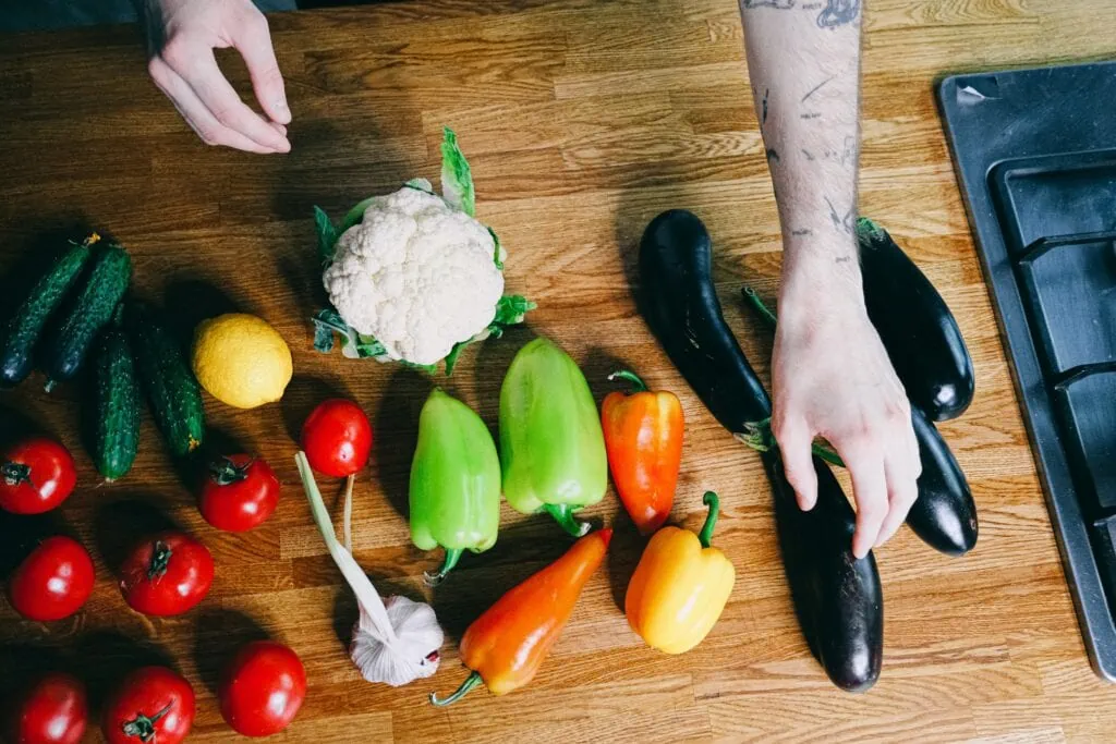 A kitchen counter full of fresh fruits and vegetables with a pair of hands outstretched.
