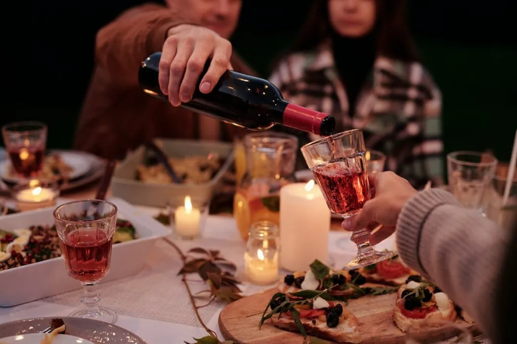 A man pouring red wine for someone across the table at a garden party.