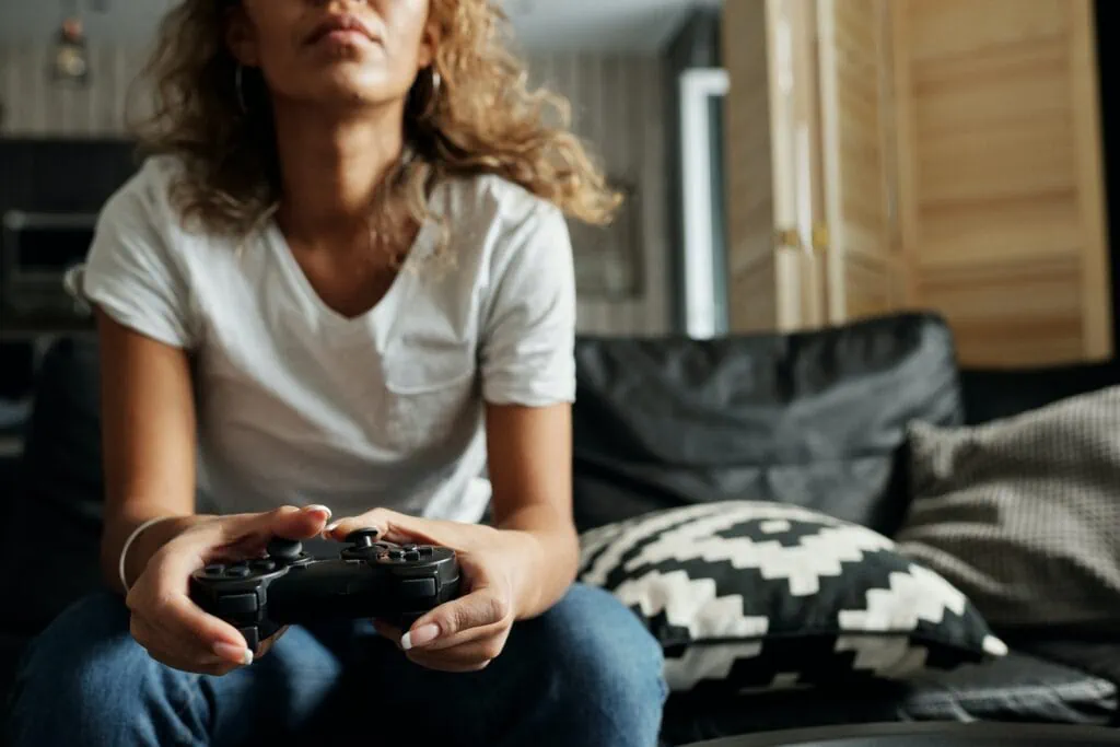 Woman with a game controller sitting on a couch; only the bottom half of her face is seen.