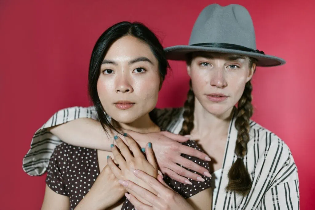 Two queer partners, one in a flat-brimmed hat with her hands around the other.