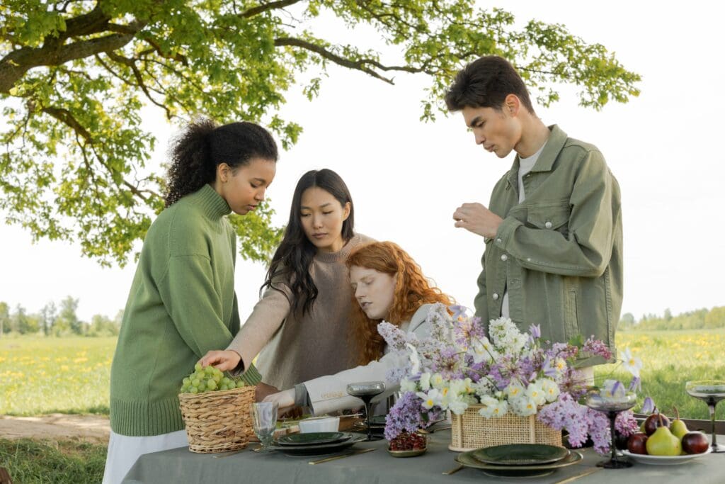 A polyamorous quad outside at a park with a beautiful spread of fruit and flowers in front of them.