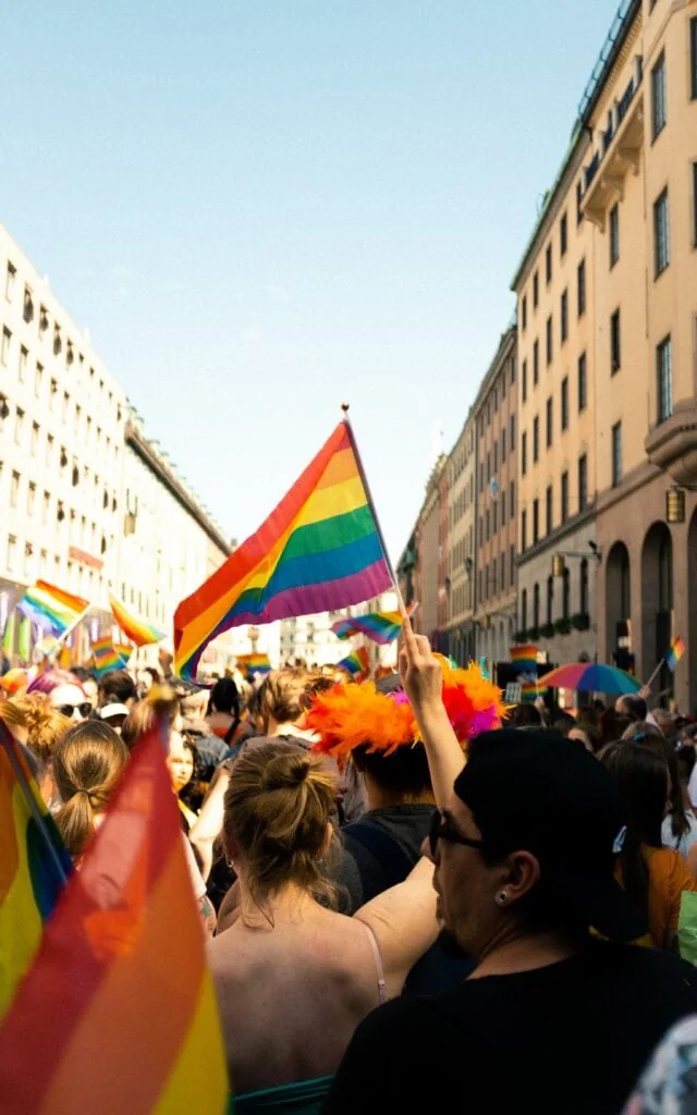 A woman holding a pride flag in the middle of a sunny parade.