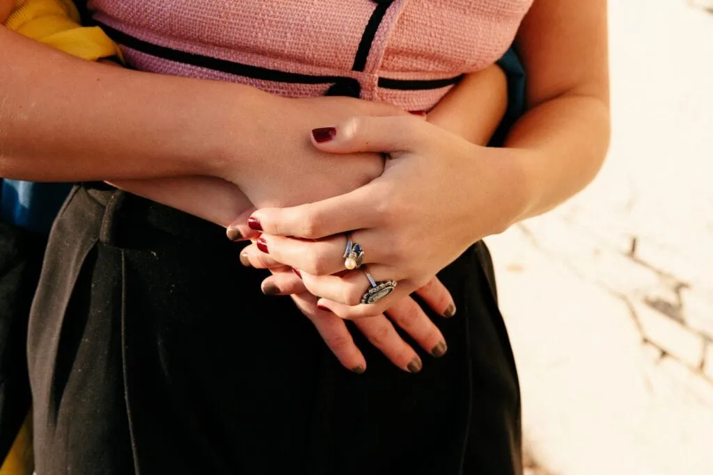 A close-up photo of two queer adults on a date, one woman’s hands around the other’s waist, intertwined.